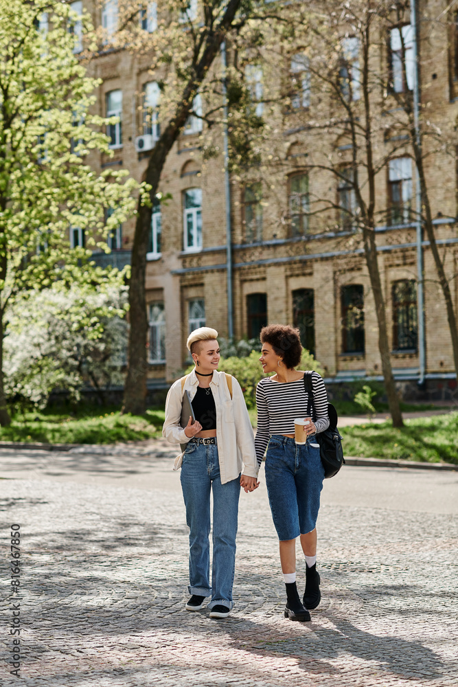 Two young women, a multicultural lesbian couple, strolling down a city street near a university campus in stylish attire.