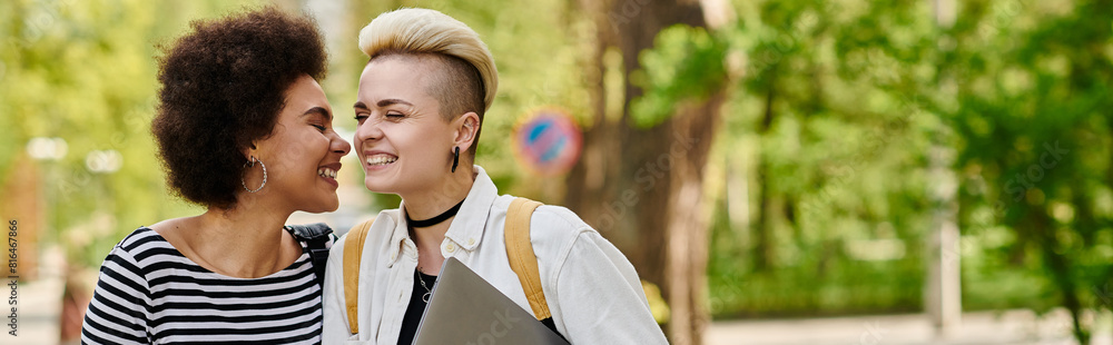 Naklejka premium Multicultural lesbian couple in casual attire walking near university campus.
