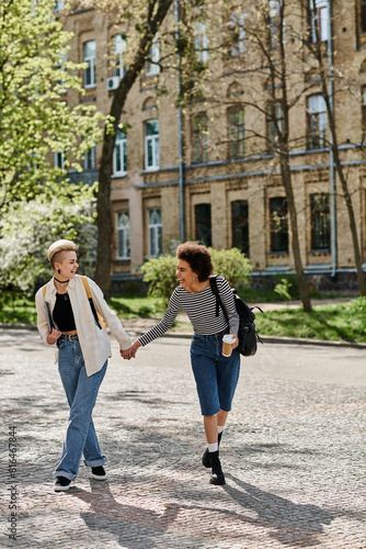 Two young women  holding hands  walk down a cobblestone street near a university campus.