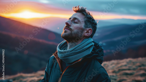 A calm handsome man in his thirties with his eyes closed and arms outstretched, breathing the fresh air on a mountain hill at sunrise © boxstock production