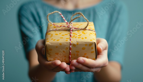 Closeup of a woman's hands presenting a festive polkadotted wrapped gift, symbolizing generosity for national give something away day against a blurred teal background photo
