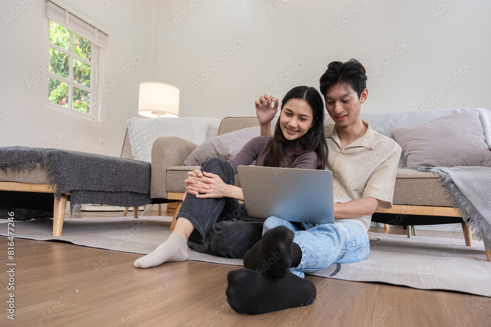 Young Asian couple in love Sitting happily together looking at laptop and relaxing in the living room. Couple making romantic love in the living room Young Asian couple in love Sitting happily together looking at laptop and relaxing in the living room. Couple making romantic love in the living room