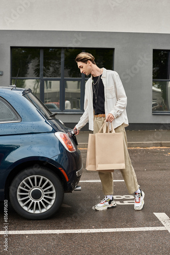 A young queer man in stylish attire stands next to a luxury car holding shopping bags. © Bliss