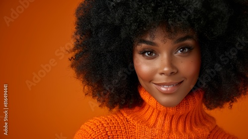  A tight shot of a person in an orange sweater and a large black afro, beaming with a broad smile
