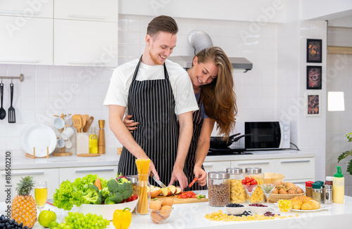 Young loving couple cooking together in the kitchen at home. Male cutting apple fruit in the kitchen, girl hugging her guy. Healthy Dieting Food Concept.