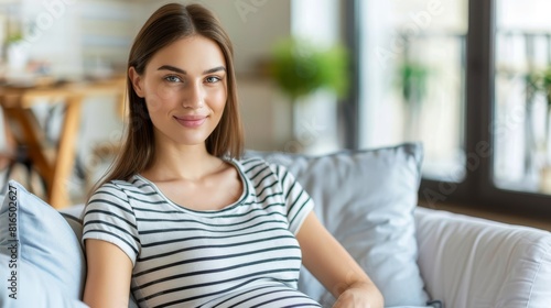 Free Download  A young woman gracefully sits on a pristine white couch Nearby, a blue pillow invites relaxation A small table holds a potted plant, adding vibrancy to the scene - GFXLoad