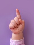 The hand of a small child shows one finger up. A small baby hand on a purple background.