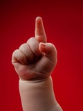 The hand of a small child shows one finger up. A small baby hand on a red background.