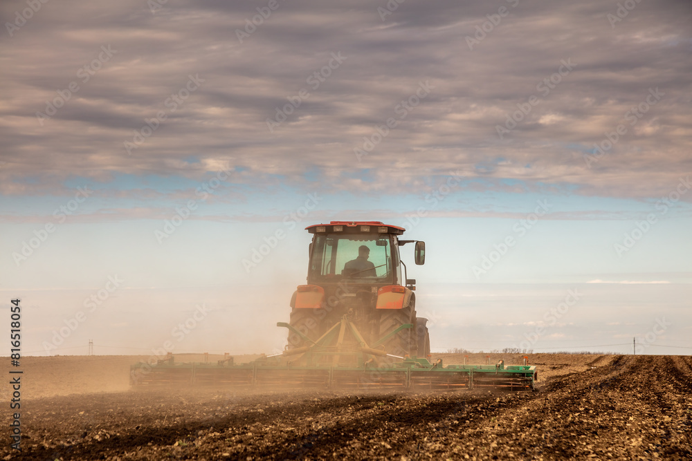 Fototapeta premium Powerful tractor tills the soil, preparing the land for planting under a dramatic sky