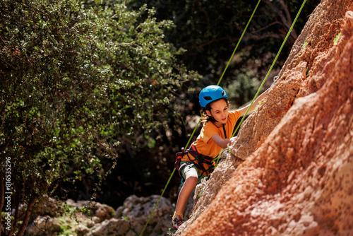 child is rock climbing at a summer camp. rock climber boy. sport in nature. cute teenager climbs a rock with a belay. active holidays.