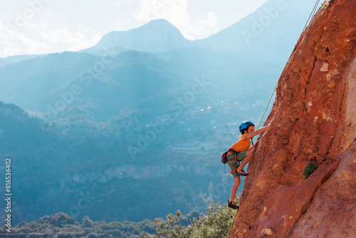 rock climber boy. sport in summer camp. a child is rock climbing at a summer camp. sport in nature on a sunny day. cute teenager climbs a rock with a belay. active holidays.