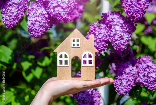 The girl holds in her hand the symbol of the house against the background of blooming lilac