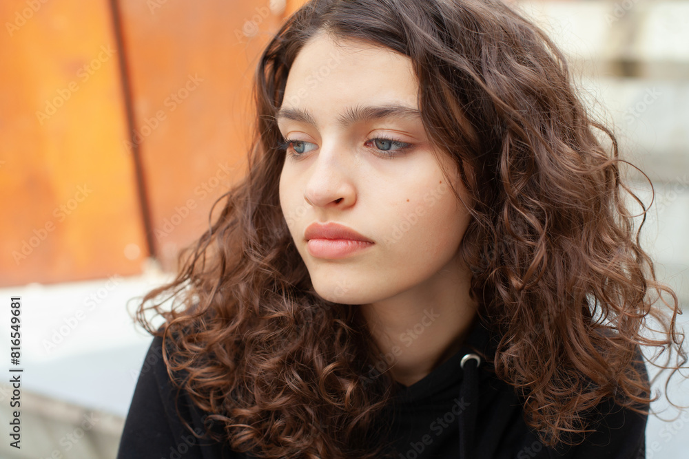 White brunette teenage girl with curly hair poses on the street in the city. White brunette teenage girl with curly hair poses on the street in the city.