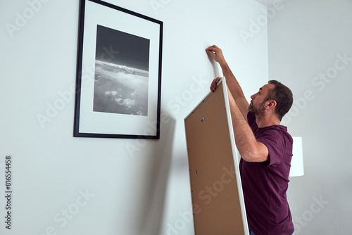 Man hanging pictures on the wall, cleaning and remodeling apartment.
