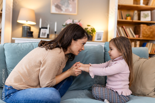 In a heartwarming scene, a young mom and her daughter, a little girl, share a cozy moment on the living room sofa. Their smiles radiate love and joy as they bond 