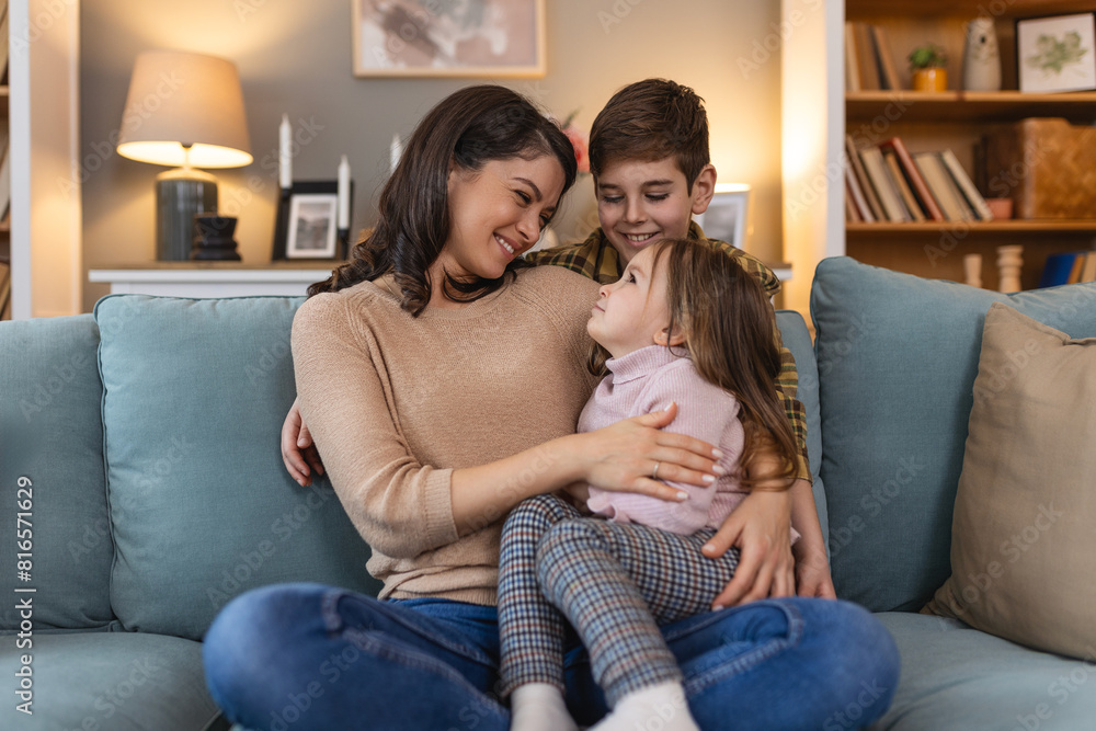 Mother shares a tender moment with her children. With her daughter and son by her side on the sofa. Their smiles speak volumes of the joy they find in each other's company