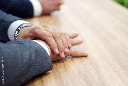 Businessman, politician or official has his hands folded while sitting at a wooden conference table. Meeting participant. Tension and suppressed anxiety. No face. Photo. Selective focus