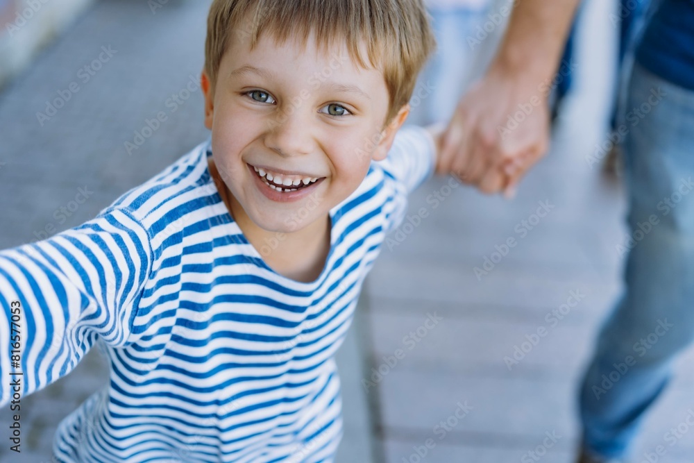 happy smiling caucasian boy waring striped sailor vest holding dad's hand walking on pavement in the city. Father's day concept happy smiling caucasian boy waring striped sailor vest holding dad's hand walking on pavement in the city. Father's day concept