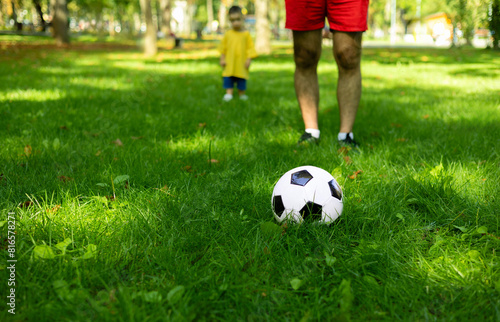 boy kid playing football in park on grass.child with ball in hands lying on ground.siblings, brothers and father,dad and son,playing together. balloon under man arm.getting ready for championship