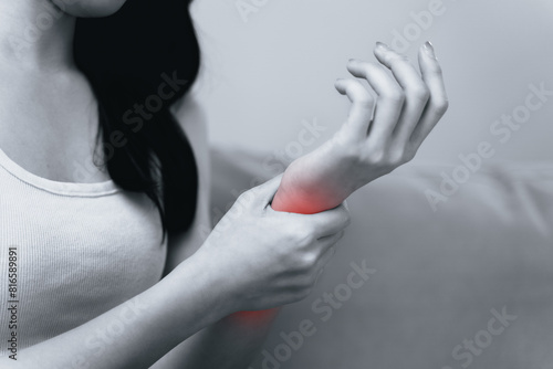 Closeup of woman sitting on sofa holds her wrist, hand injury with red highlight photo