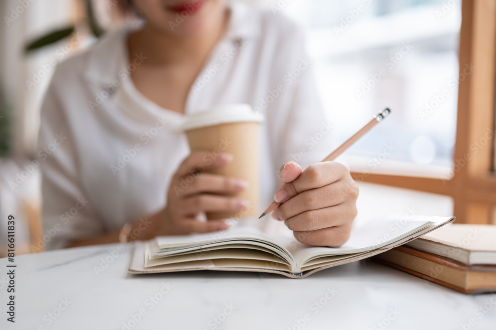 A cropped shot of a woman writing something in her notebook while sitting in a coffee shop. A cropped shot of a woman writing something in her notebook while sitting in a coffee shop.