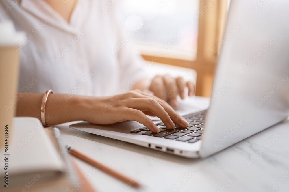 A close-up image of a woman typing on keyboard, working on the computer at a table in a coffee shop.