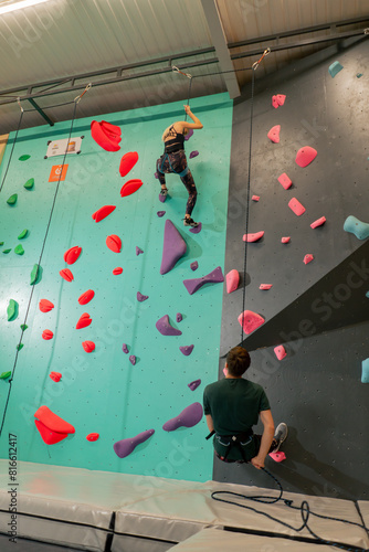 at the climbing wall young girl climbs the wall for the first time, the coach belays with a safety rope