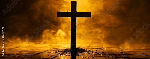 A close-up of a cross on wet ground illuminated by a yellow light, with smoke swirling around. The scene evokes a dramatic, atmospheric effect with a touch of mystique. photo