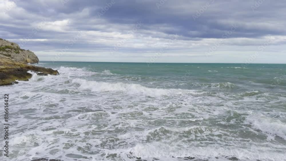Strong wind in spring on the Mediterranean Sea off the coast of Spain. The waves splash against the rocks. Trees sway in the wind. Benicassim. Castellon Strong wind in spring on the Mediterranean Sea off the coast of Spain. The waves splash against the rocks. Trees sway in the wind. Benicassim. Castellon