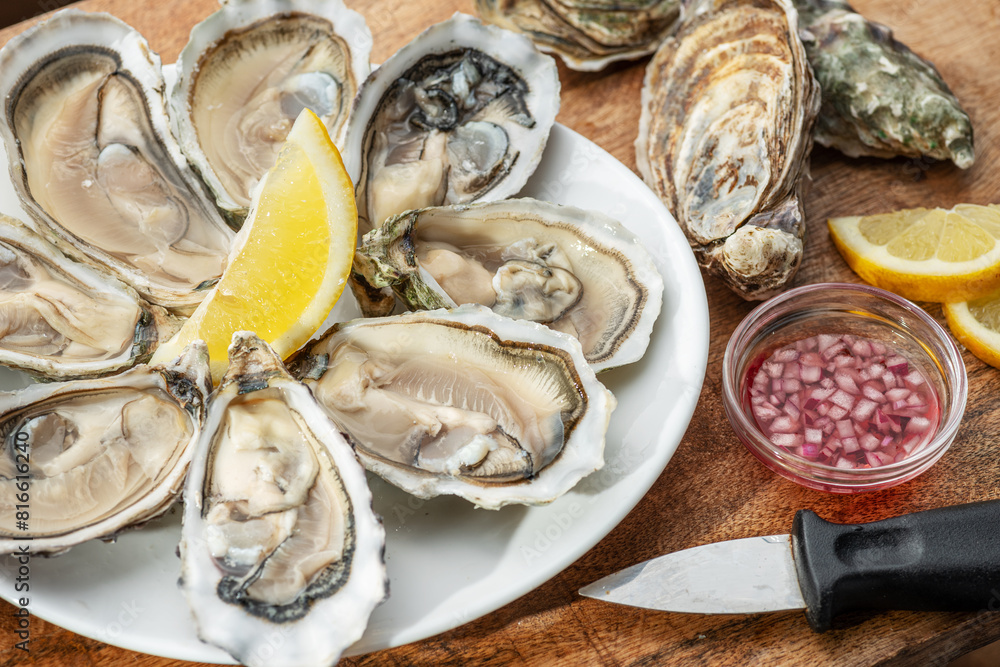 Opened raw oysters with sauce and lemon slices on plate on wooden table. Top view. Opened raw oysters with sauce and lemon slices on plate on wooden table. Top view.