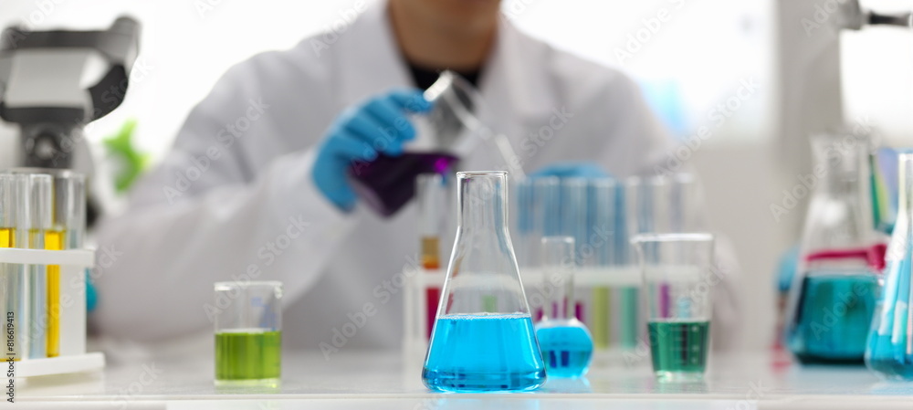 Male chemist holds test tube of glass in his hand overflows a liquid solution of potassium permanganate conducts an analysis reaction takes various versions of reagents using chemical manufacturing. Male chemist holds test tube of glass in his hand overflows a liquid solution of potassium permanganate conducts an analysis reaction takes various versions of reagents using chemical manufacturing.