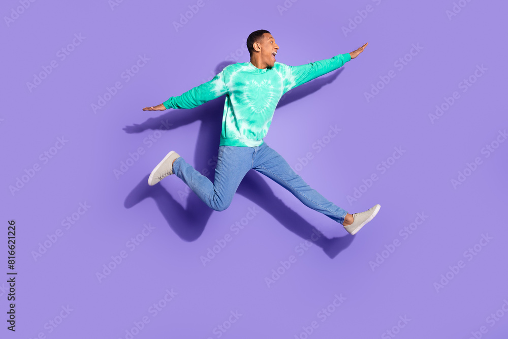 Full length photo of handsome good mood guy wear teal sweatshirt jumping high emtpy space isolated purple color background Full length photo of handsome good mood guy wear teal sweatshirt jumping high emtpy space isolated purple color background
