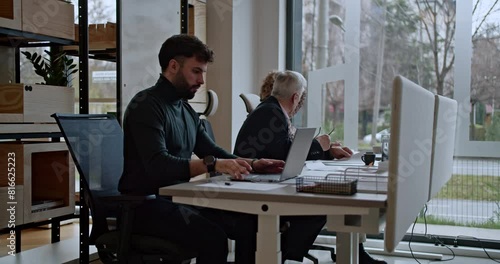 Young man and older colleagues working on their respective tasks at a well-lit office table, exemplifying productivity and concentration in a contemporary workspace.