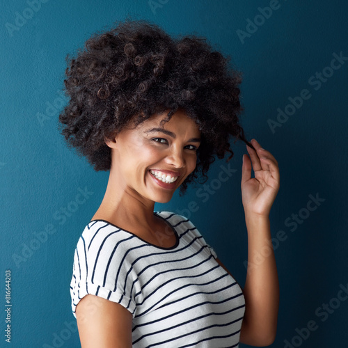 Woman  portrait and pull curly hair in studio with confidence for growth  results or smile by blue background. African person  girl and model with care  happy or transformation with cosmetic for afro