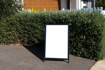 A blank white mockup background texture of a signboard against a garden tree hedge fence. Empty A-Frame Signs with copy space. Street advertisement easel stand.