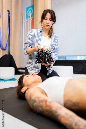 Vertical photo of a woman using an instrument to do sound therapy in a gym room. Concept of somatic seeds. Bull's-eye seeds for sound massages.