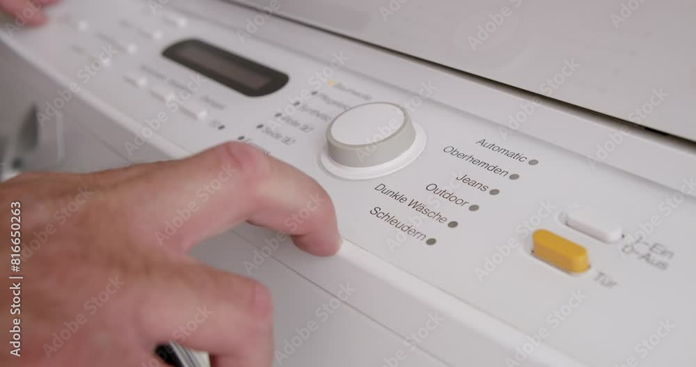 A mans hand is seen selecting a program on a household washing machine, likely preparing to do laundry. A mans hand is seen selecting a program on a household washing machine, likely preparing to do laundry.