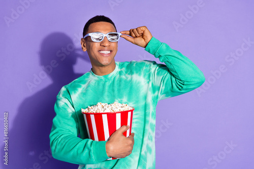 Photo of attractive funny guy wear teal sweatshirt enjoy film eat pop corn isolated purple color background
