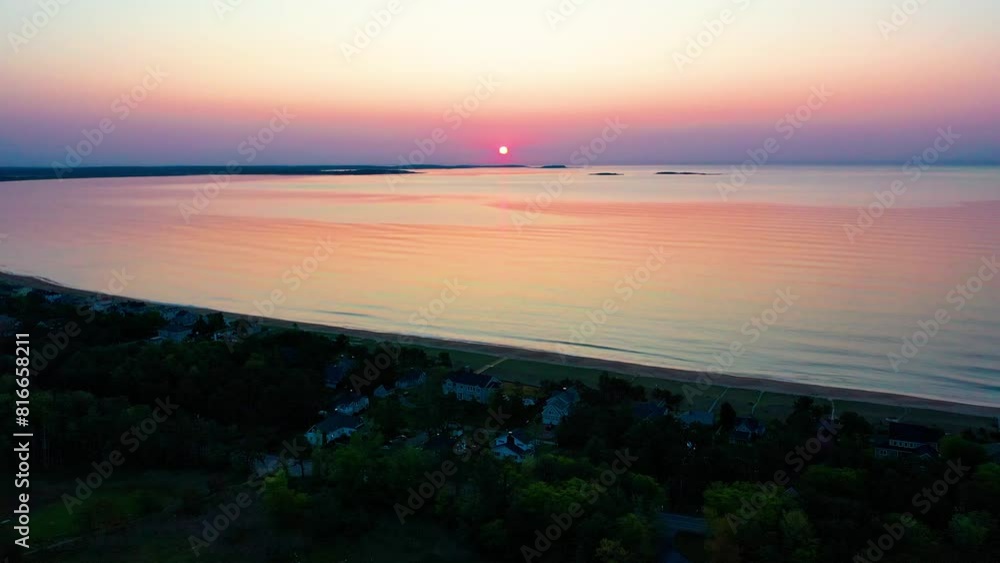 Aerial Drone View of Sunset over Beach Houses with Colorful Reflections off Ocean Waves and Vacation Homes Along the New England Atlantic Coastline. Colorful Golder Hour Bright Glowing Sky and Sea Aerial Drone View of Sunset over Beach Houses with Colorful Reflections off Ocean Waves and Vacation Homes Along the New England Atlantic Coastline. Colorful Golder Hour Bright Glowing Sky and Sea