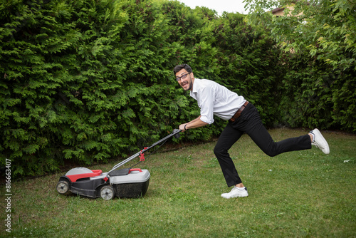 Cheerful businessman mowing the lawn with a lawnmower in the backyard. Leisure and household concept	