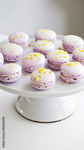 Lavender macarons, each adorned with a lemon sprinkle. The macaroons are artfully arranged on a pristine white cake stand, set against a minimalist white backdrop. Copy space