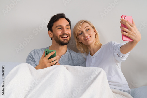 Happy playful couple making video conference stream.Girl taking portrait picture of her boyfriend husband shoot selfie photo by cellphone cell phone cellular smartphone. Man and woman have fun at home