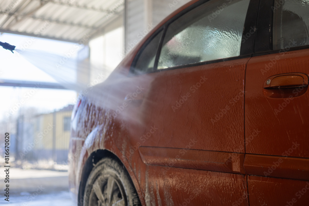 Side view of a man rinsing his car with water at a car wash. A man came to a car wash where he could wash his car himself using powerful water pistols.