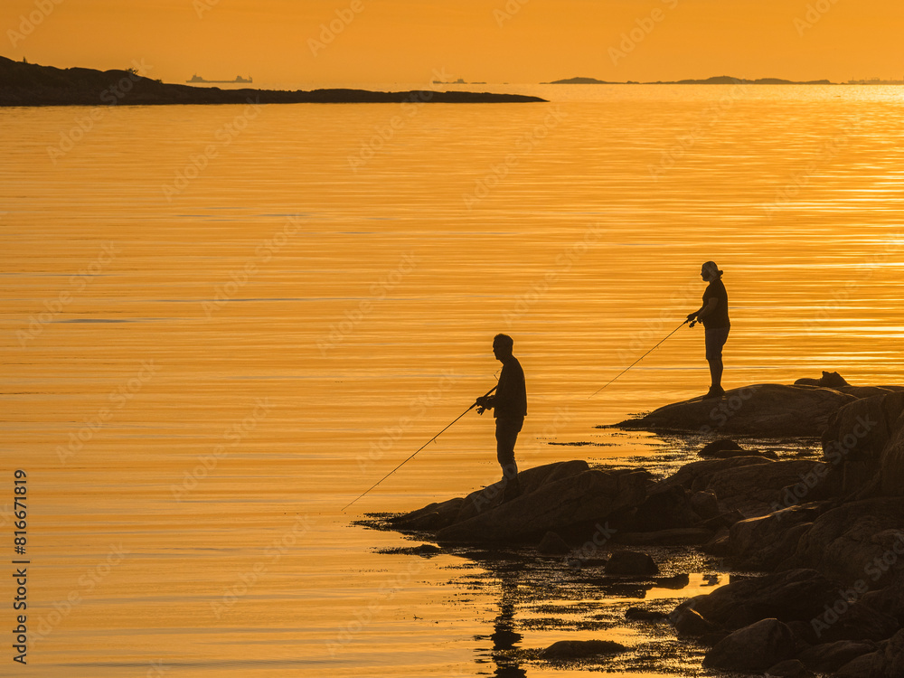 Naklejka premium Men Fishing From a Cliff at Sunset in Swedens Serene Seascape