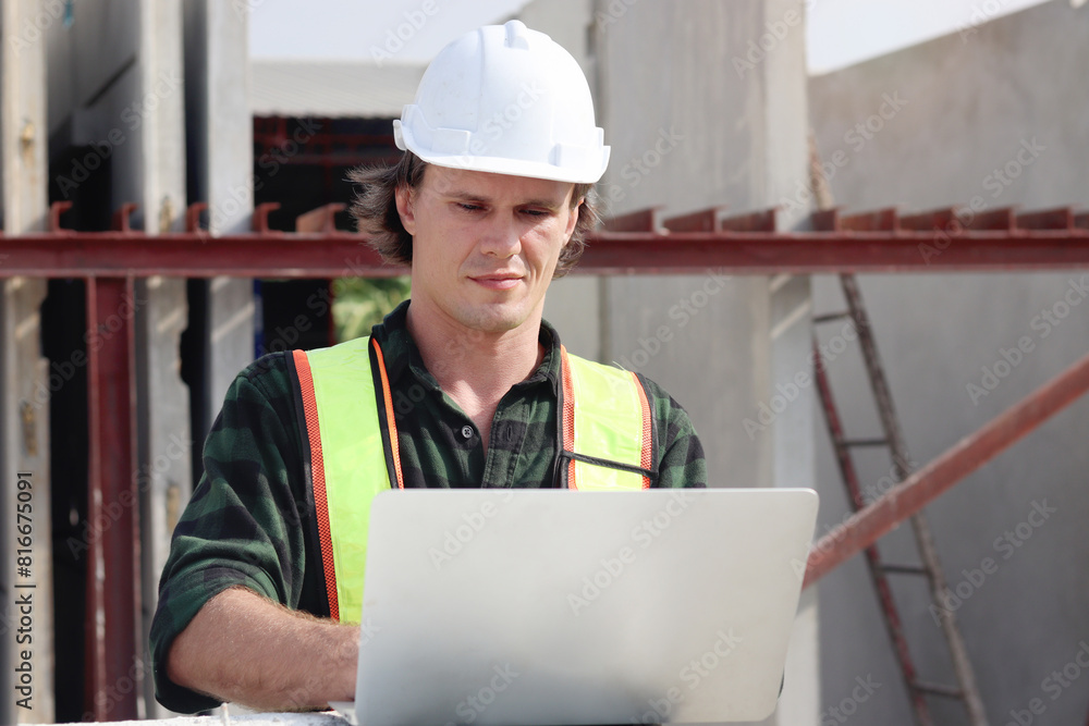 Happy worker engineer with safety vest and helmet typing on laptop computer while inspecting working area at construction building site. Young architect works at building site workplace. Happy worker engineer with safety vest and helmet typing on laptop computer while inspecting working area at construction building site. Young architect works at building site workplace.