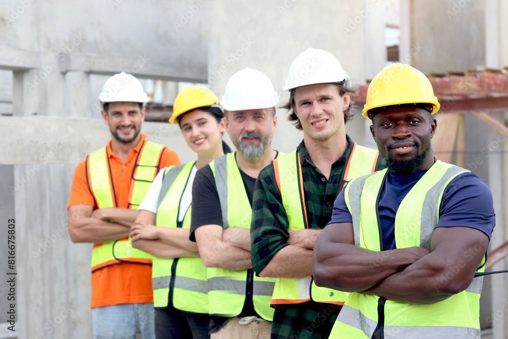 Group of happy engineer worker team with safety vest and helmet standing with arms crossed in line at construction building site. Construction labor work at workplace. Teamwork unity and diversity