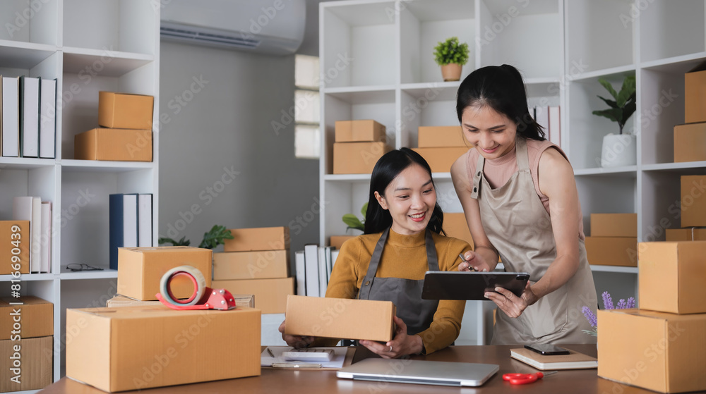 Two Asian women packing boxes and using a tablet in a home office. Concept of small business and e-commerce. Two Asian women packing boxes and using a tablet in a home office. Concept of small business and e-commerce.
