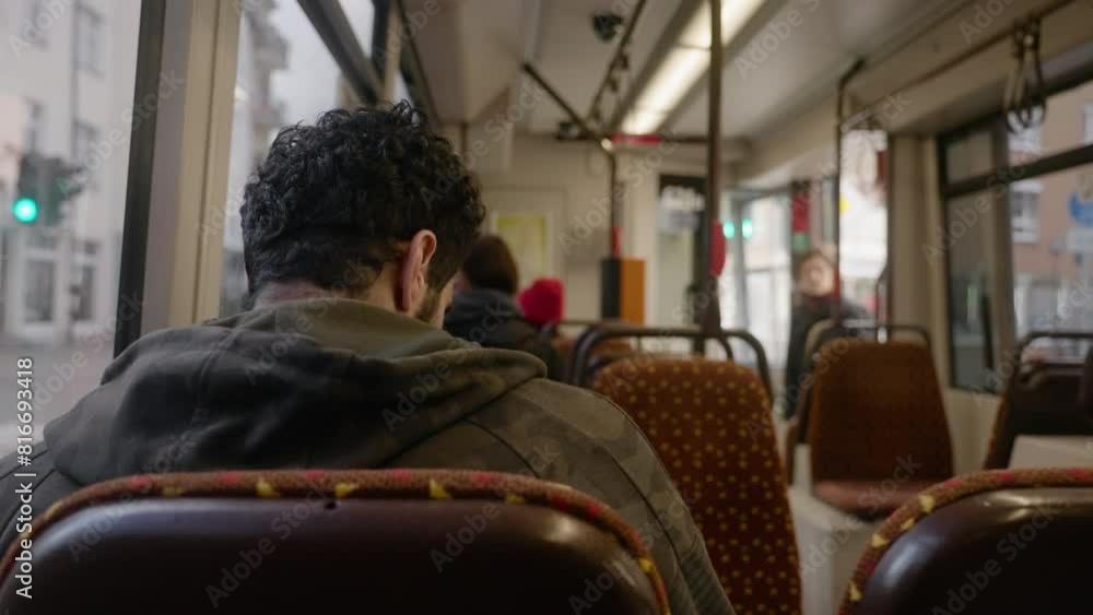 Back shot of an adult man sitting in a tramway with a passenger getting on in the blur background Back shot of an adult man sitting in a tramway with a passenger getting on in the blur background