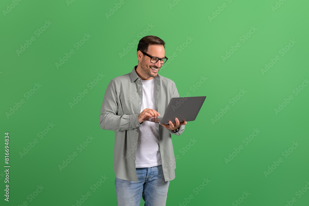 Portrait of happy handsome entrepreneur checking e-mails online over laptop against green background Portrait of happy handsome entrepreneur checking e-mails online over laptop against green background