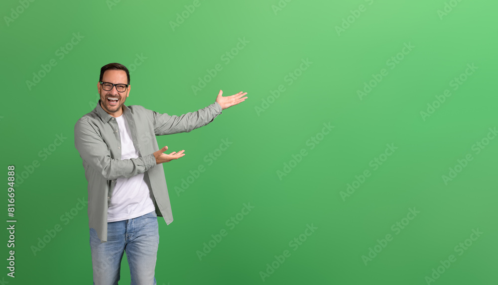 Young businessman laughing and presenting new product on empty space over isolated green background Young businessman laughing and presenting new product on empty space over isolated green background